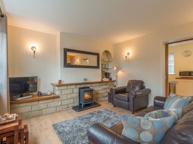A living room with leather armchairs a rug a small stove and a television at Crumstone Corner in Seahouses