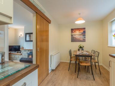 A dining room with a wooden table and four chairs a painting on the wall and a sliding wooden door leading to a living room at Crumstone Corner in Seahouses