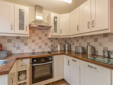 A kitchen with white cabinets wooden countertops electric stove oven toaster and kettle at Crumstone Corner in Seahouses