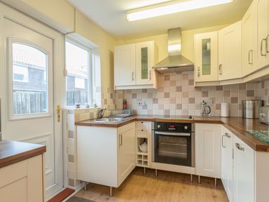 A kitchen with white cabinets wooden countertops an oven a sink and a door leading outside at Crumstone Corner in Seahouses