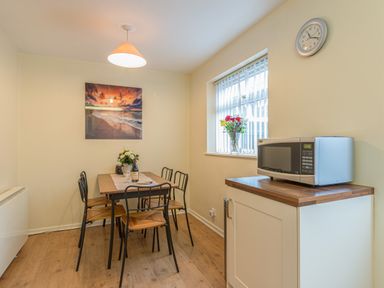 A dining area with a table and chairs a microwave on a counter and flowers in a window at Crumstone Corner in Seahouses