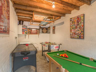 A game room with a pool table, air hockey table, foosball table, dart board, and comic book wall art at Crumstone Corner in Seahouses