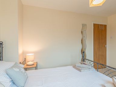 A bedroom with a bed a bedside table with a lamp a wavy wall mirror and a wooden door at Crumstone Corner in Seahouses