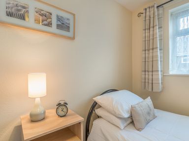 A bedroom with a single bed pillows and a nightstand with a lamp and clock at Crumstone Corner in Seahouses