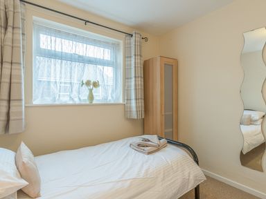 A bedroom with a single bed a window with curtains a wardrobe and a decorative wall mirror at Crumstone Corner in Seahouses