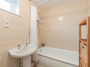 A bathroom with a bathtub shower combination and a white sink with taps at Crumstone Corner in Seahouses