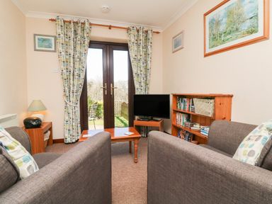 A sitting room with two sofas a wooden coffee table a TV and bookshelves at Honeysuckle Cottage in Bude