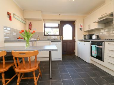 A kitchen with wooden chairs a countertop with flowers a dishwasher a door and various appliances at Honeysuckle Cottage in Bude
