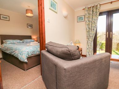 A bedroom with a bed next to a living area with a sofa and glass doors at Honeysuckle Cottage in Bude