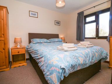 A bedroom with a double bed bedside tables and lamps a wardrobe and window with curtains at Honeysuckle Cottage in Bude
