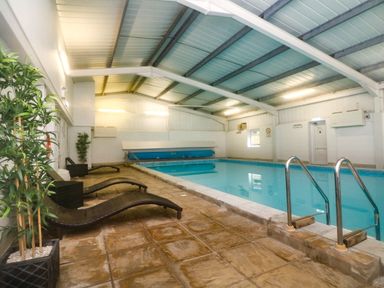 An indoor swimming pool with lounge chairs and potted plants at Honeysuckle Cottage in Bude