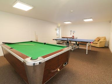 A game room with a pool table and a ping pong table and an armchair at Honeysuckle Cottage in Bude
