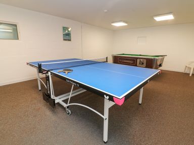 A game room with a blue ping pong table and a pool table in the background at Honeysuckle Cottage in Bude