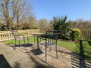 An outdoor patio with two metal chairs and a round table surrounded by a wooden fence and plants at Honeysuckle Cottage in Bude