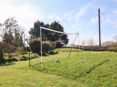 A soccer goal with two balls on a grassy field surrounded by trees and a fence at Honeysuckle Cottage in Bude