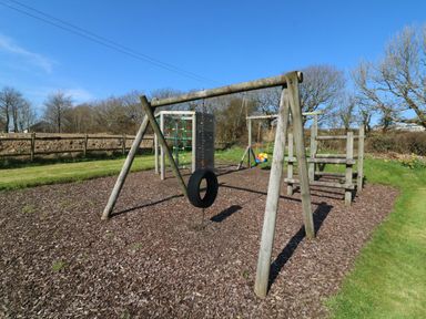 A playground with a tire swing climbing frame and child swing outdoors at Honeysuckle Cottage in Bude
