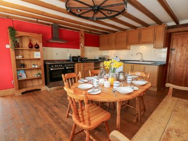 A kitchen with wooden dining table set for breakfast wooden chairs wooden cabinets and a wooden shelf at The Farmhouse in Aberaeron
