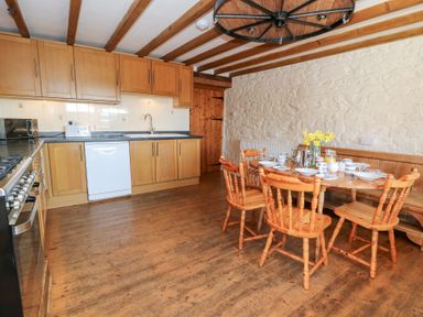 A kitchen with wooden cabinets a dining table with chairs and a stone wall at The Farmhouse in Aberaeron
