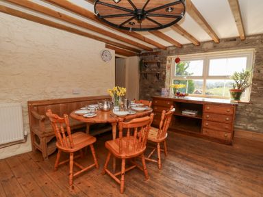 A dining area with a round wooden table set for four and wooden chairs next to a window and wooden sideboard at The Farmhouse in Aberaeron