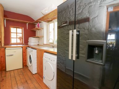 A laundry room with washing machine dryer fridge and iron on shelves at The Farmhouse in Aberaeron