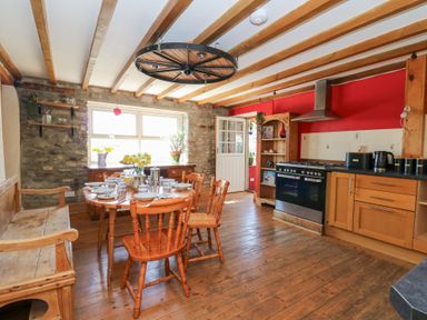 A kitchen with wooden dining table and chairs wooden bench stove and shelves at The Farmhouse in Aberaeron