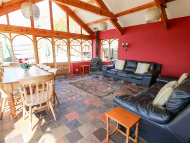 A sunroom with a wooden dining table and chairs leather sofas a wood stove and tiled floor at The Farmhouse in Aberaeron