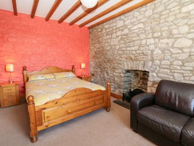 A bedroom with a wooden bed with yellow bedding a stone fireplace and a dark leather armchair at The Farmhouse in Aberaeron