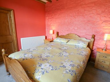A bedroom with a wooden bed with floral bedding and two bedside tables with lamps at The Farmhouse in Aberaeron