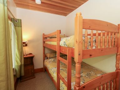 A small bedroom with wooden bunk beds and a nightstand with a lamp at The Farmhouse in Aberaeron