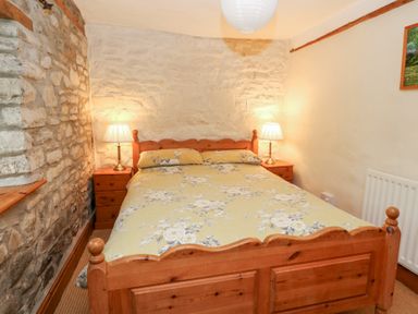 A bedroom with a wooden double bed flanked by two wooden nightstands with lamps against a stone wall at The Farmhouse in Aberaeron