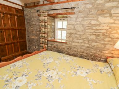 A bedroom with a floral yellow bedspread stone walls a small window and wooden wardrobe at The Farmhouse in Aberaeron