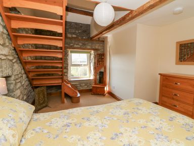 A bedroom with a wooden staircase stone wall wooden dresser and a bed with floral bedding at The Farmhouse in Aberaeron