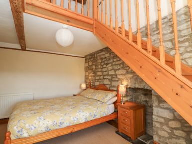 A bedroom with a bed under wooden stairs and stone wall at The Farmhouse in Aberaeron