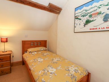 A bedroom with a wooden bed with floral bedding a wooden nightstand with a lamp and a framed picture on the wall at The Farmhouse in Aberaeron