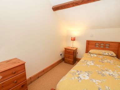 A bedroom with a single bed yellow floral bedding wooden bedside and chest of drawers at The Farmhouse in Aberaeron