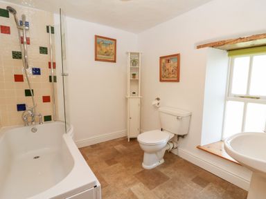 A bathroom with a bathtub shower combination toilet sink and bookshelf near a window at The Farmhouse in Aberaeron