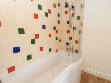 A bathtub with a showerhead and colorful square tiles on the wall at The Farmhouse in Aberaeron