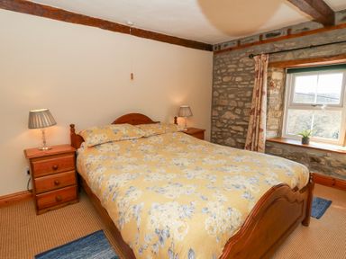 A bedroom with a wooden bed and nightstands with lamps by a window with curtains at The Farmhouse in Aberaeron