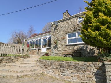 Stone house with steps leading to a door and a wooden bench near a tree at The Farmhouse in Aberaeron