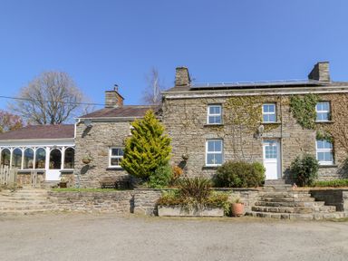A stone house with a white door surrounded by plants and steps at The Farmhouse in Aberaeron