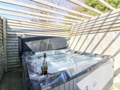 An outdoor hot tub with two glasses and a bottle under a wooden pergola at The Farmhouse in Aberaeron