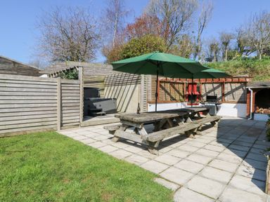 A fenced patio area with two picnic tables and green umbrellas a barbecue a hot tub and wood storage at The Farmhouse in Aberaeron
