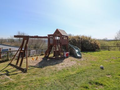 A wooden playground set with swings and a slide on a grassy field at The Farmhouse in Aberaeron