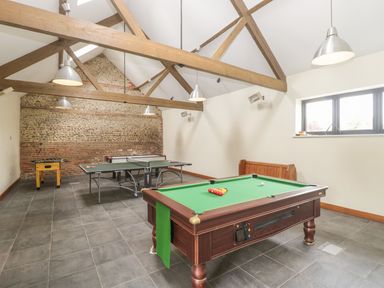 A game room with a pool table ping pong table and foosball table under wooden beams at Corner Barn in Winterborne Stickland