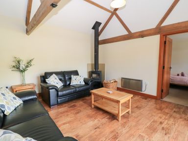 A living room with a sofa, coffee table, and stove at Corner Barn in Winterborne Stickland