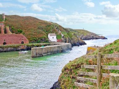 A coastal scene with a small harbor wall a boat a wooden fence and hills in the background at Ty Pren in Llanrhian near St Davids