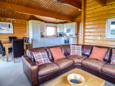 A wooden interior with a brown leather corner sofa with cushions a wooden dining table with black chairs and a white kitchen at Ty Pren Llanrhian near St Davids