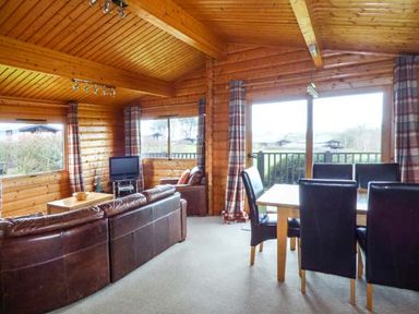 A wooden interior living room with a brown leather sofa a television and a dining table with black chairs at Ty Pren in Llanrhian near St Davids
