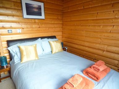 A bedroom with a bed blue bedding and orange towels on a wooden wall at Ty Pren in Llanrhian near St Davids