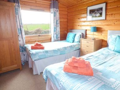 A bedroom with two single beds each with blue bedding and orange towels a wooden wardrobe and a window showing a green field at Ty Pren in Llanrhian near St Davids